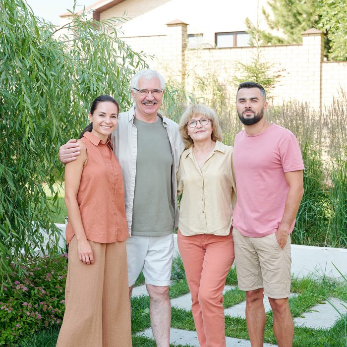 Full shot family portrait of senior parents and their young adult children standing together outdoors looking at camera